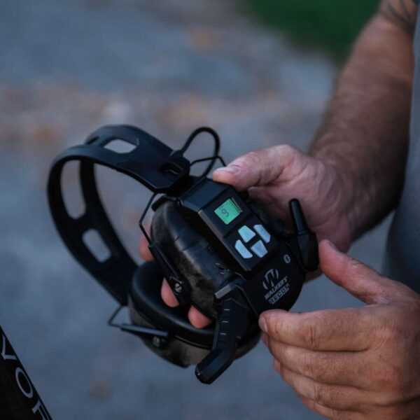 image of user with the walker's recon bluetooth walkie talkie. View is from the left side angle that showcases the digital screen and its buttons.